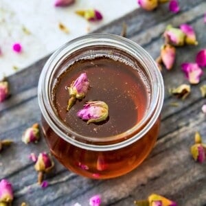 A glass bottle full of rose simple syrup with two rose petals on top of it.