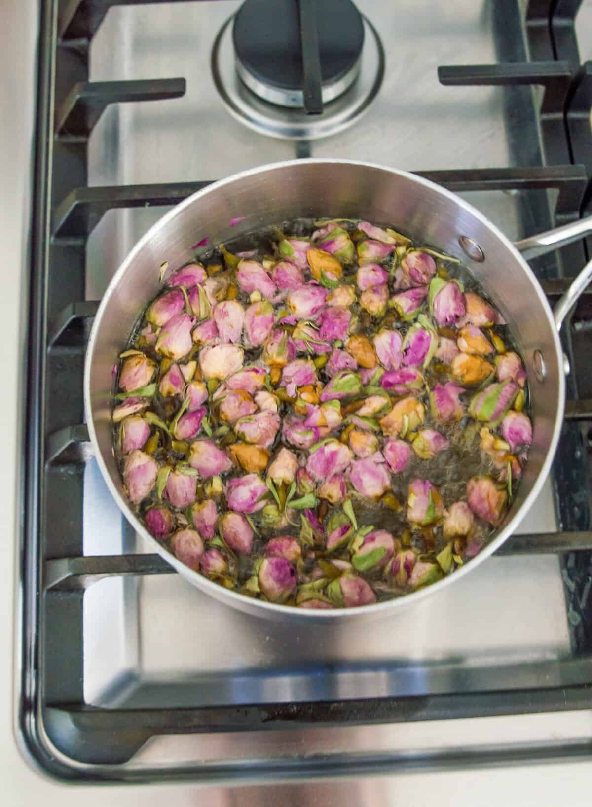 A pot on the stovetop with water, sugar and rose petals in it.