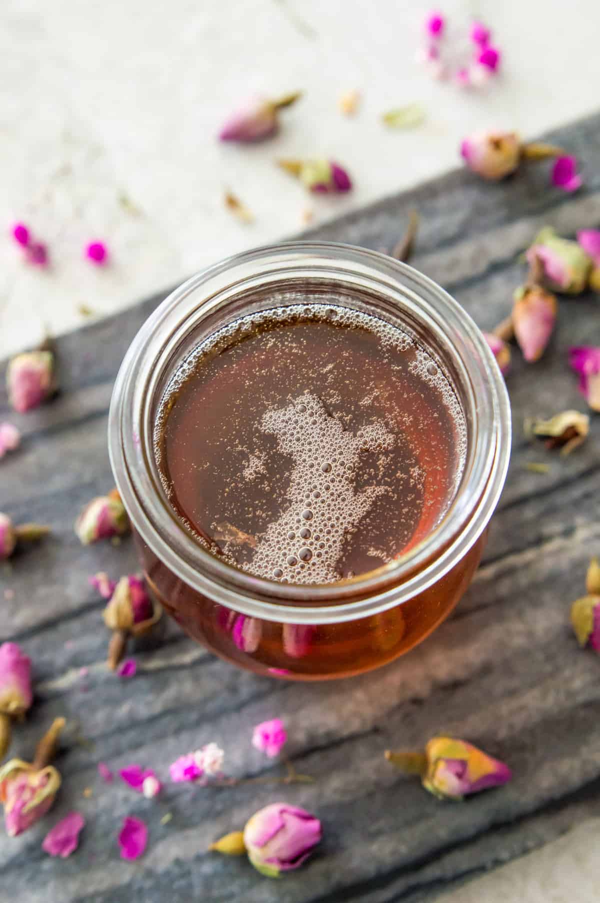 A glass jar filled with a simple syrup with rosebuds around it.