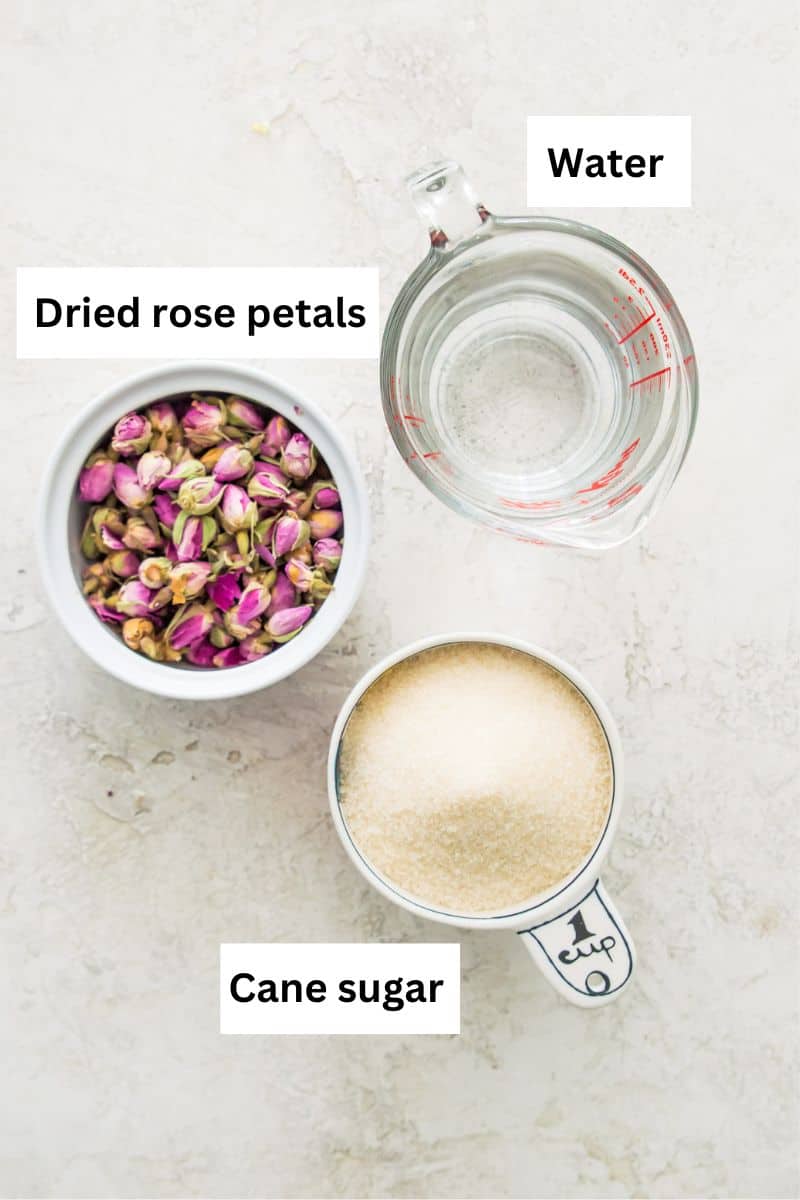 The ingredients needed to make rose simple syrup separated into bowl including water, cane sugar and dried rose petals.