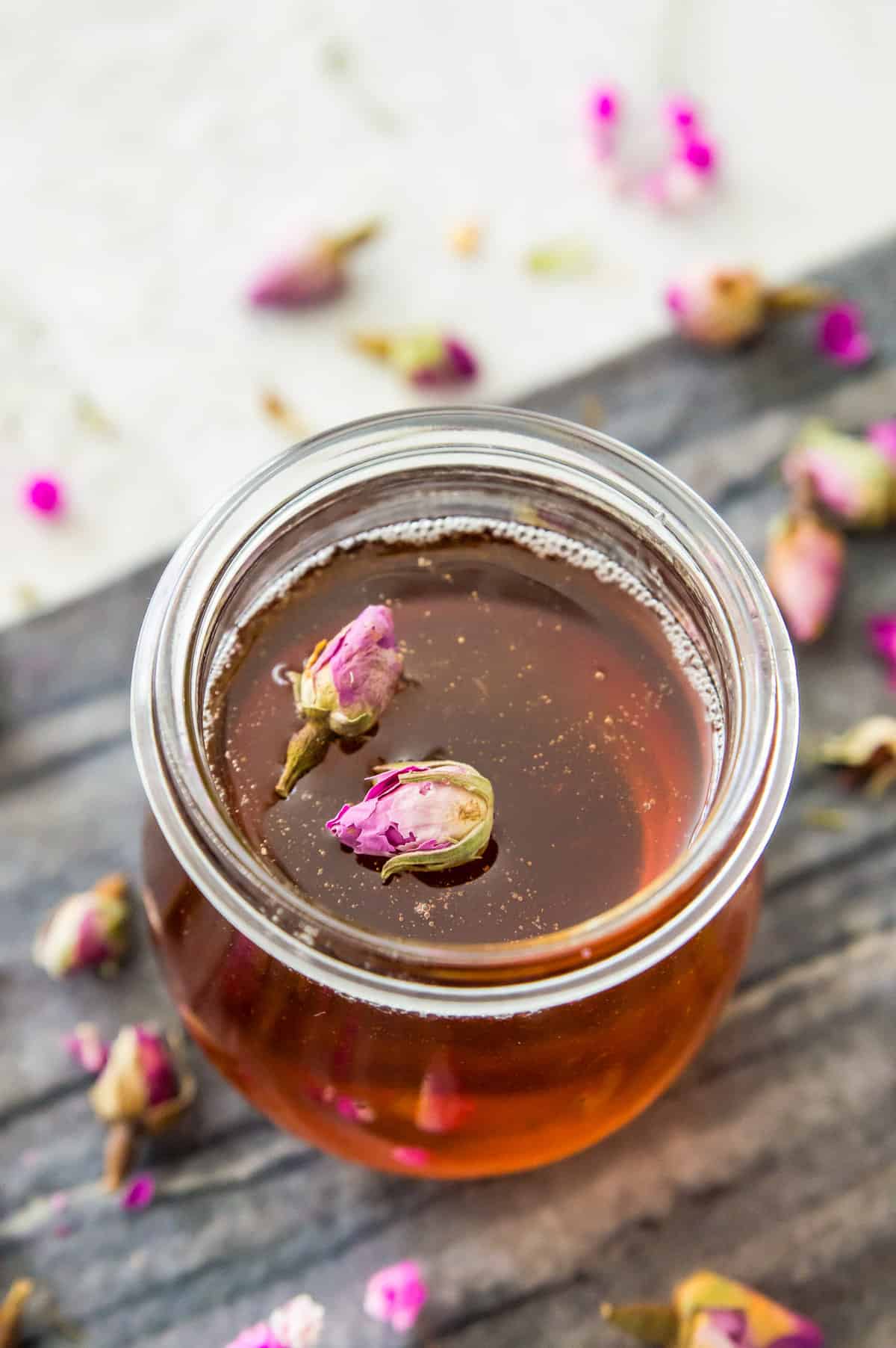 A glass jar filled with a rose simple syrup and topped with two dried rose buds.