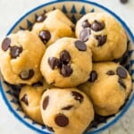 A bowl of chocolate chip cookie dough bites with chocolate chips around it.