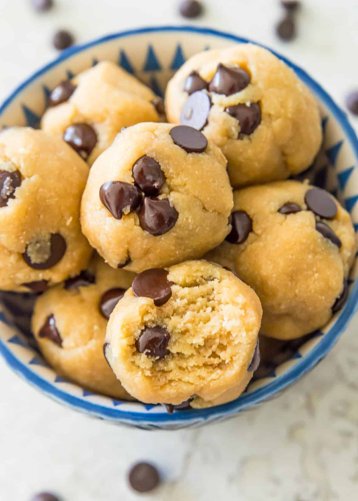 A bowl filled with no bake chocolate chip cookie dough balls and one of them has a bite out of it.