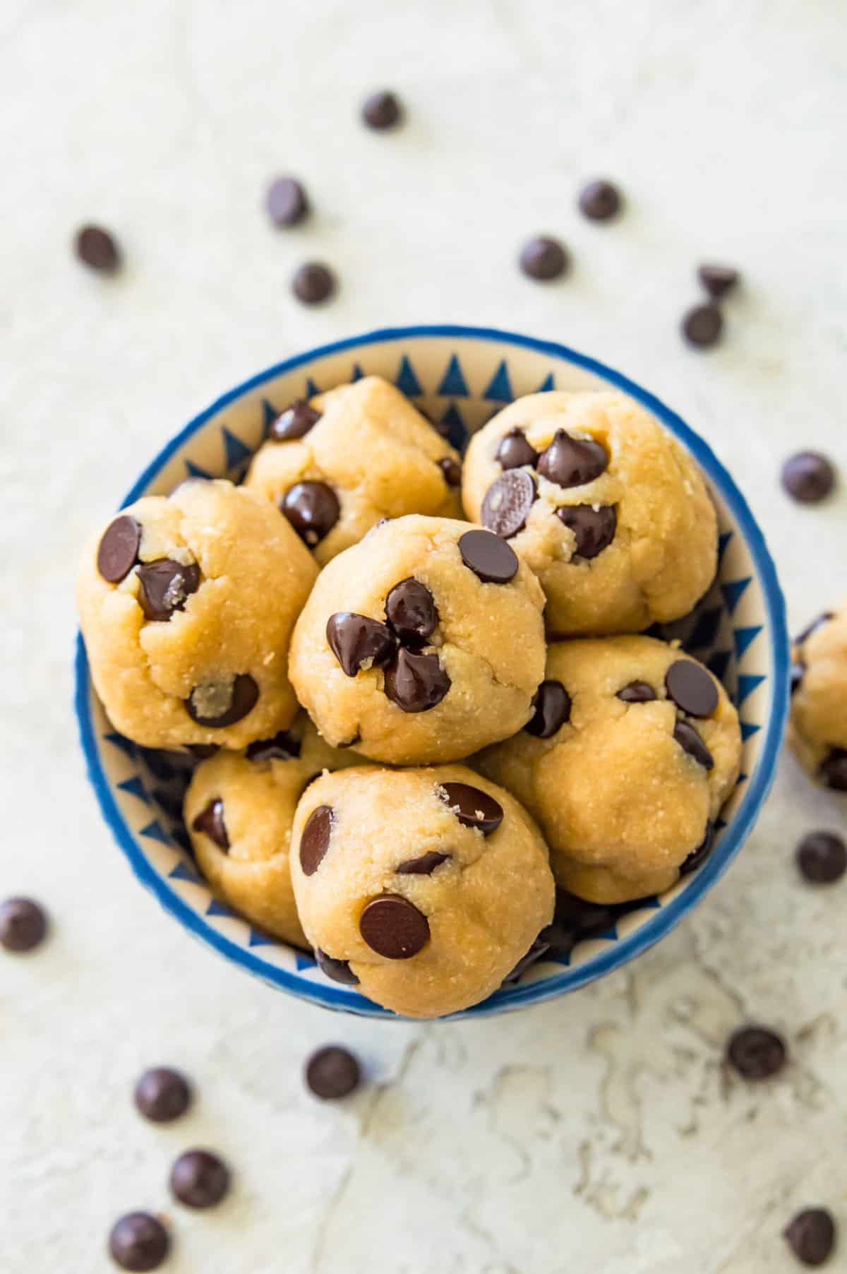 A bowl filled with no bake cookie dough bites with chocolate chips around the bowl.