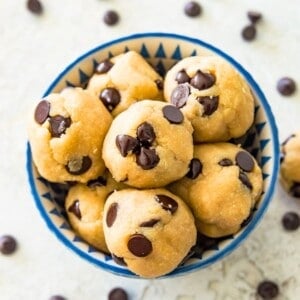 A bowl full of edible chocolate chip cookie dough bites with chocolate chips around the bowl.