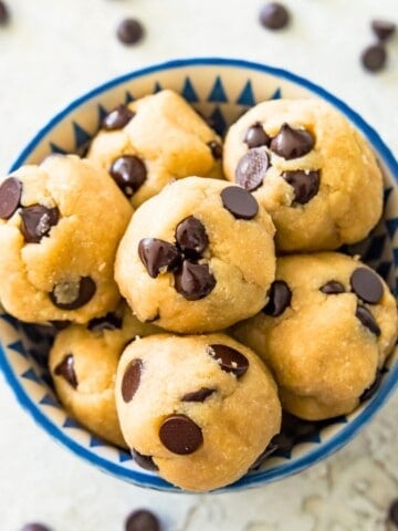 A bowl full of edible chocolate chip cookie dough bites with chocolate chips around the bowl.