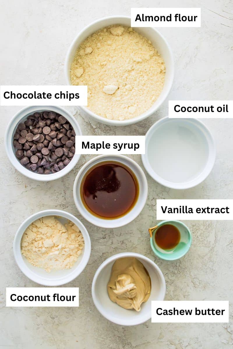The ingredients needed to make no bake chocolate chip cookie dough bites separated into bowls including almond flour, chocolate chips, cashew butter, maple syrup and vanilla extract.