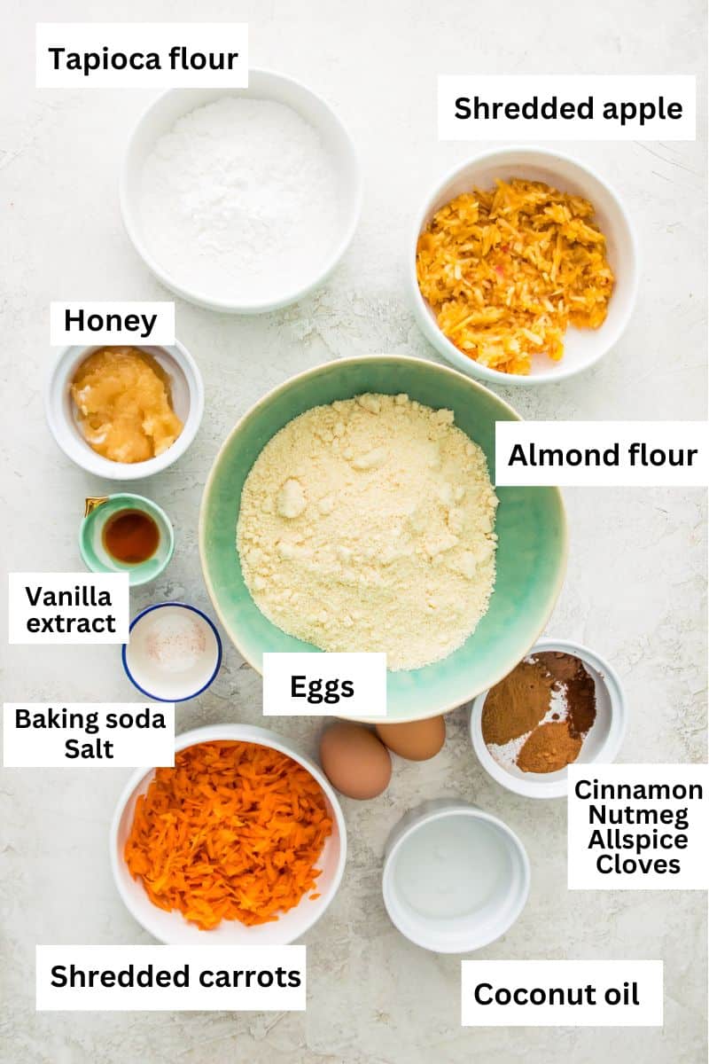 The ingredients needed to make carrot cake donuts separated into bowls including almond flour, shredded carrots, shredded apple, eggs, honey and spices. 