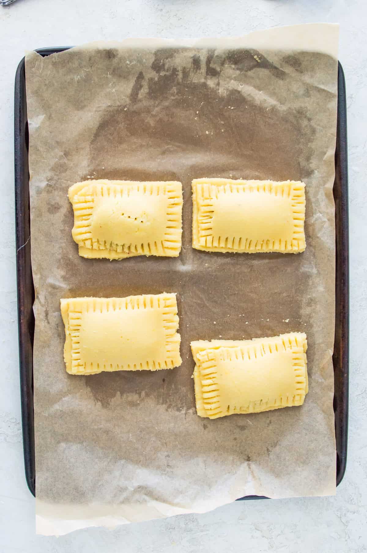 Pop tarts that have not been baked on a baking sheet lined with parchment paper. 