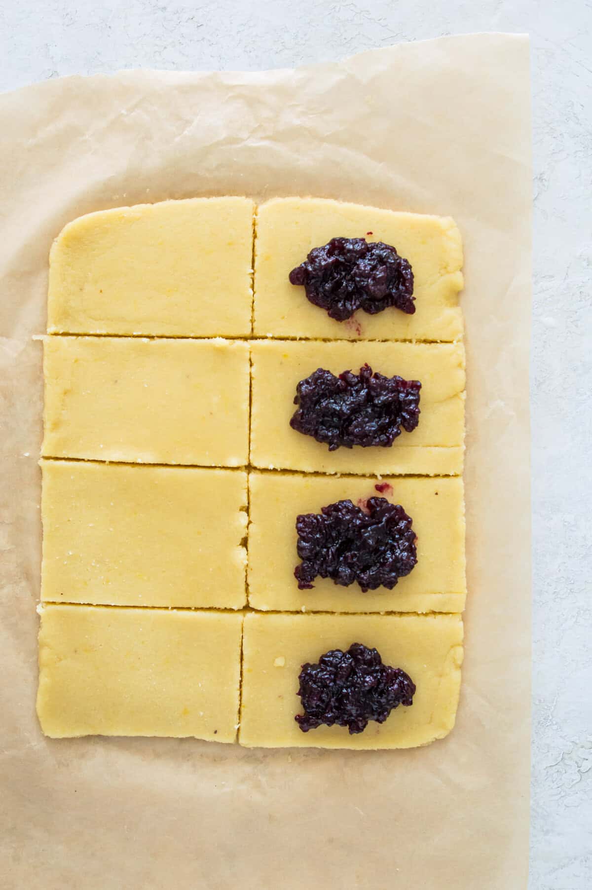 A piece of dough that has been cut into 8 evenly sized rectangles and half of them have blueberry jam on them. 