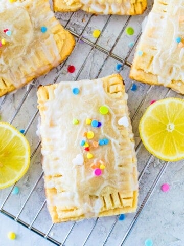 Four lemon pop tarts topped with colourful sprinkles on a wire rack with lemon slices beside them.
