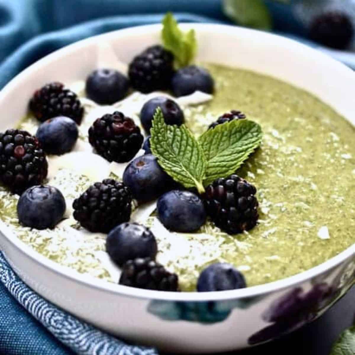 A mint smoothie bowl topped with shredded coconut, blueberries and cacao nibs.