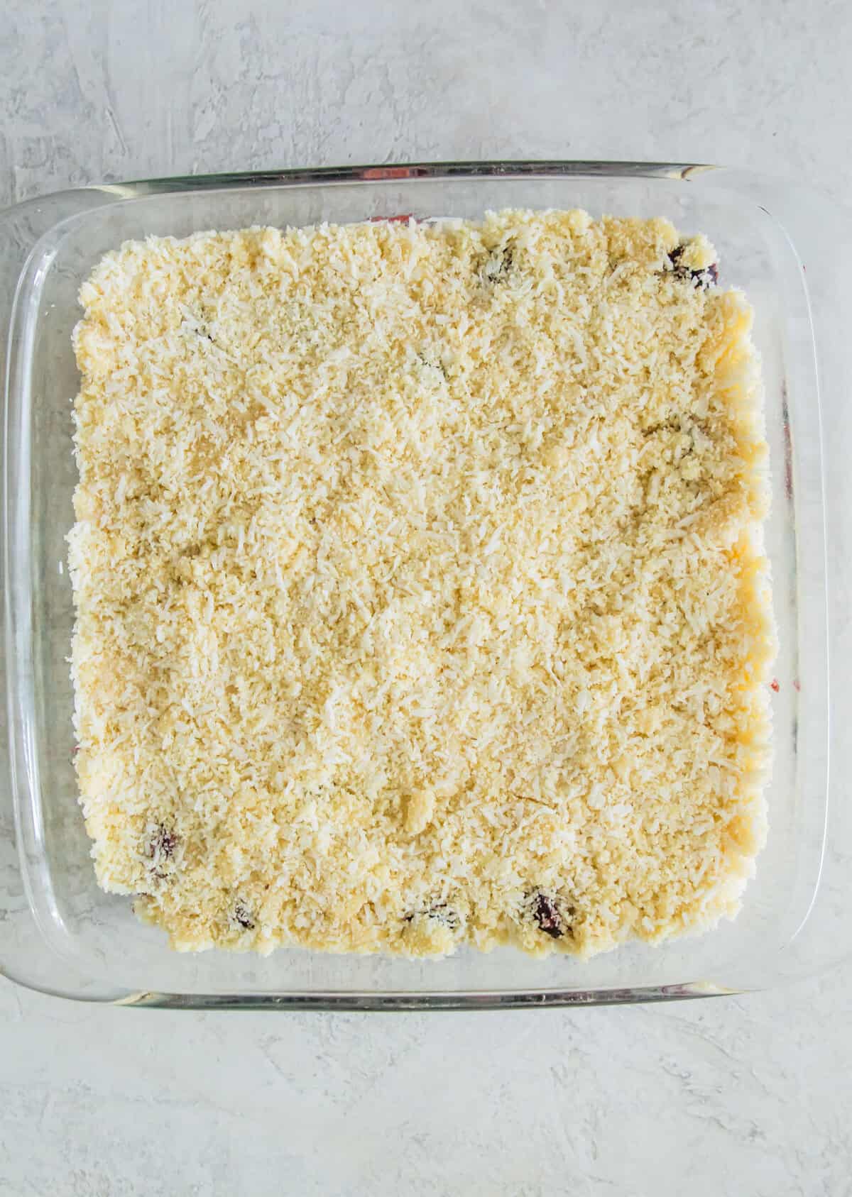 A glass baking pan with a layer of almond four and shredded coconut in it.
