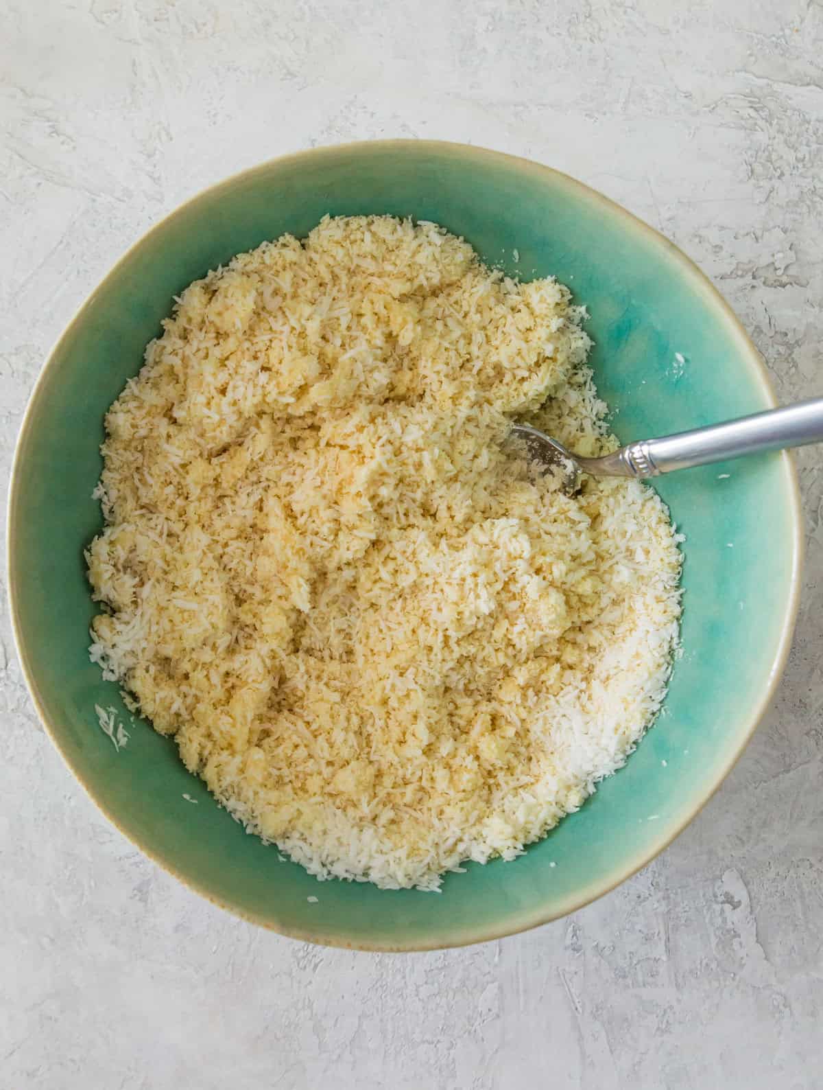 A bowl with almond flour and shredded coconut mixed together with a spoon in the mixture.
