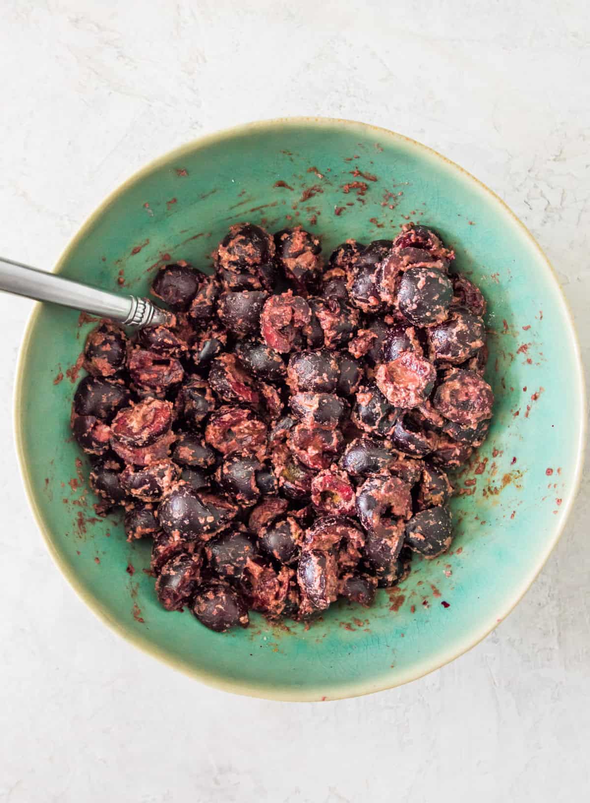 A large bowl with chopped cherries in it and a spoon in it.