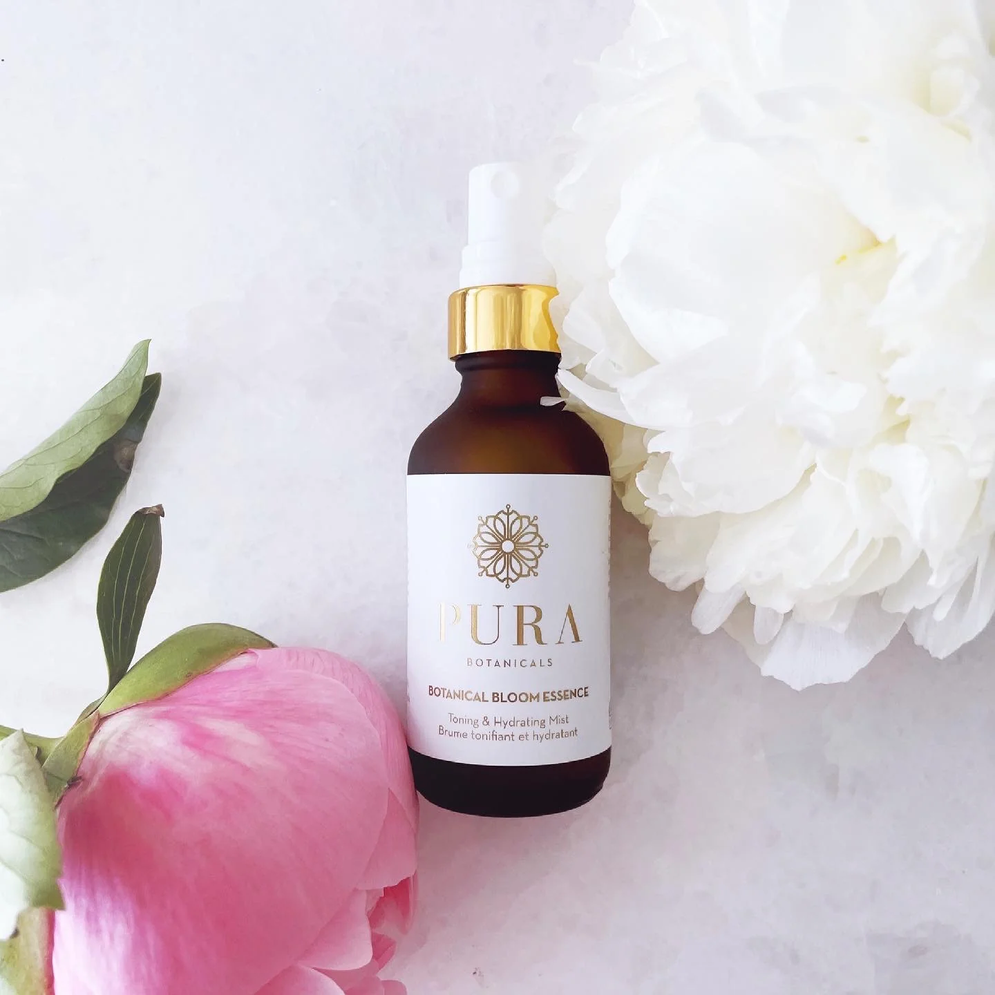 A bottle of Pura Botanicals hydrating mist with pink and white peonies around it.