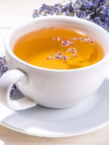 A mug of lavender tea with dried lavender flowers around it.